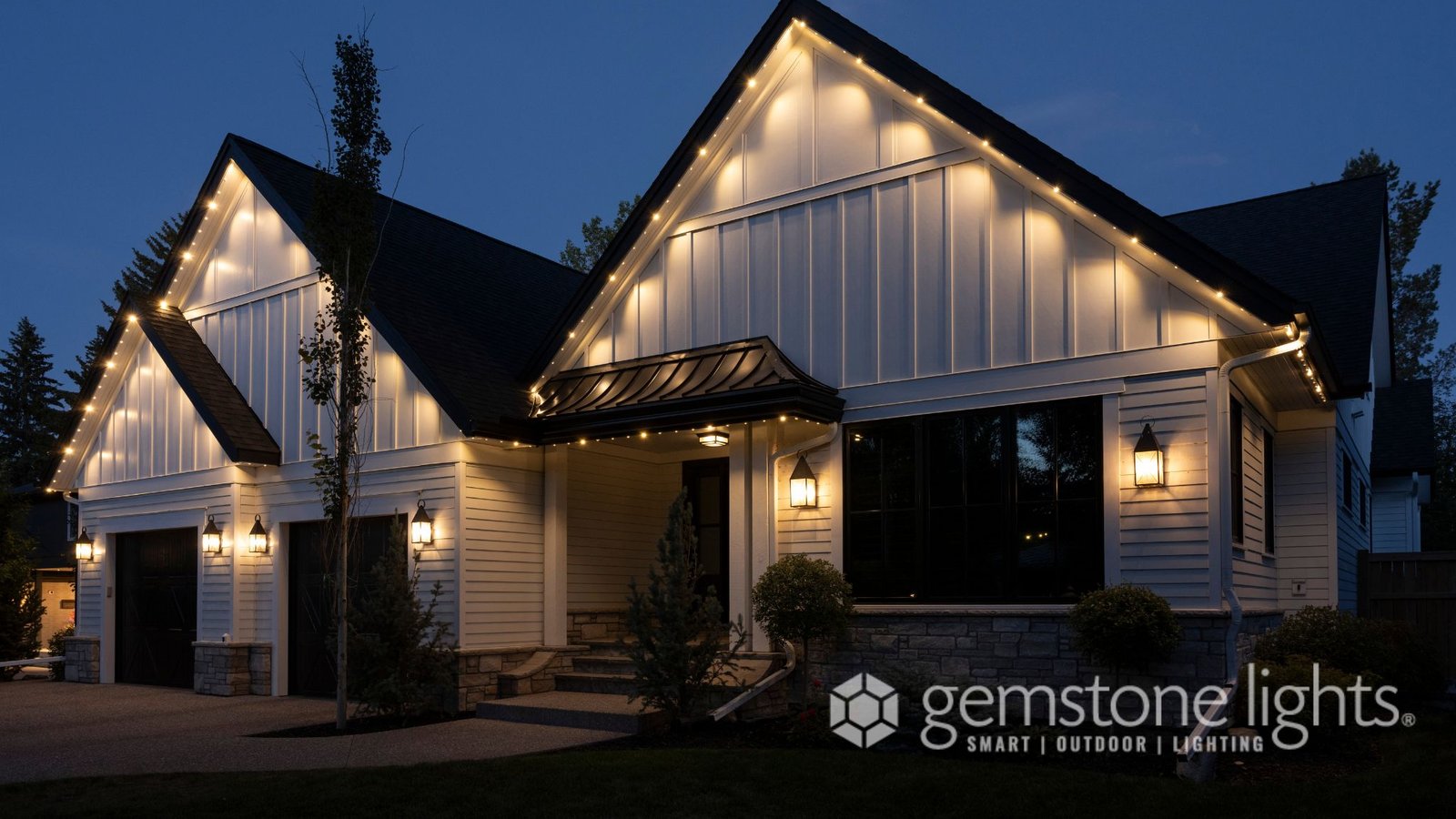 Two-story white farmhouse-style home with Gemstone permanent lighting in warm white along the rooflines at dusk