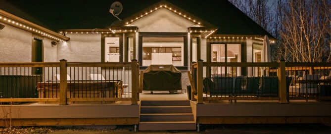 Warm white permanent lights tracing the gable and eaves above a backyard deck at night — example from an authorized Gemstone dealer gallery.