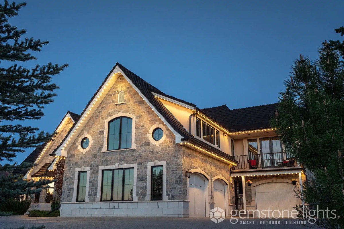 Stone home with arched windows and Gemstone permanent lighting in warm white along the roof edges at twilight